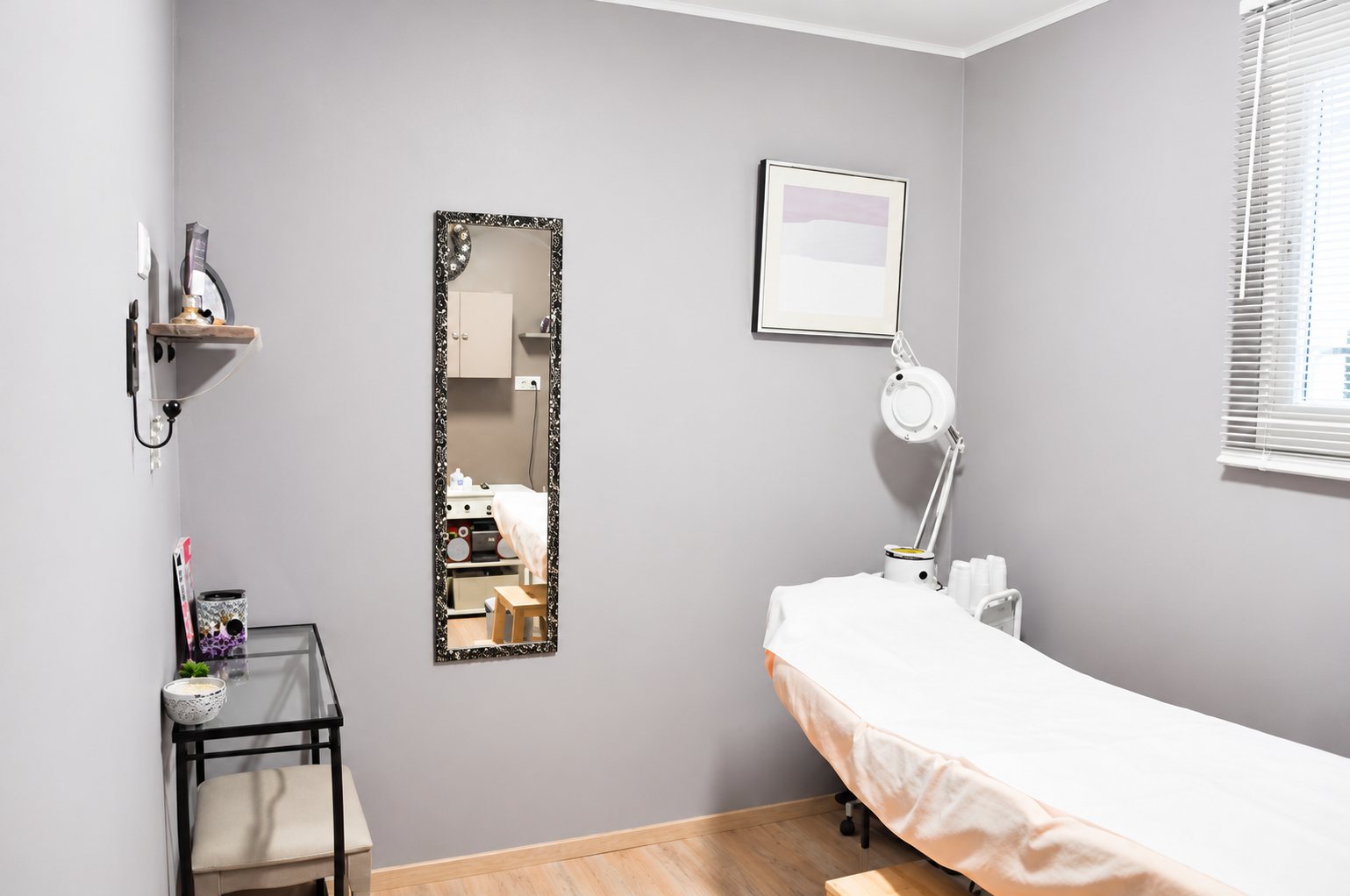 Cabine de soins aux murs gris-mauve avec table de massage et lampe loupe
