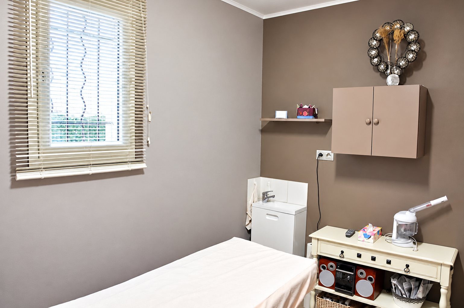 Cabine de soins aux murs taupe avec table de massage, lavabo et appareil à vapeur