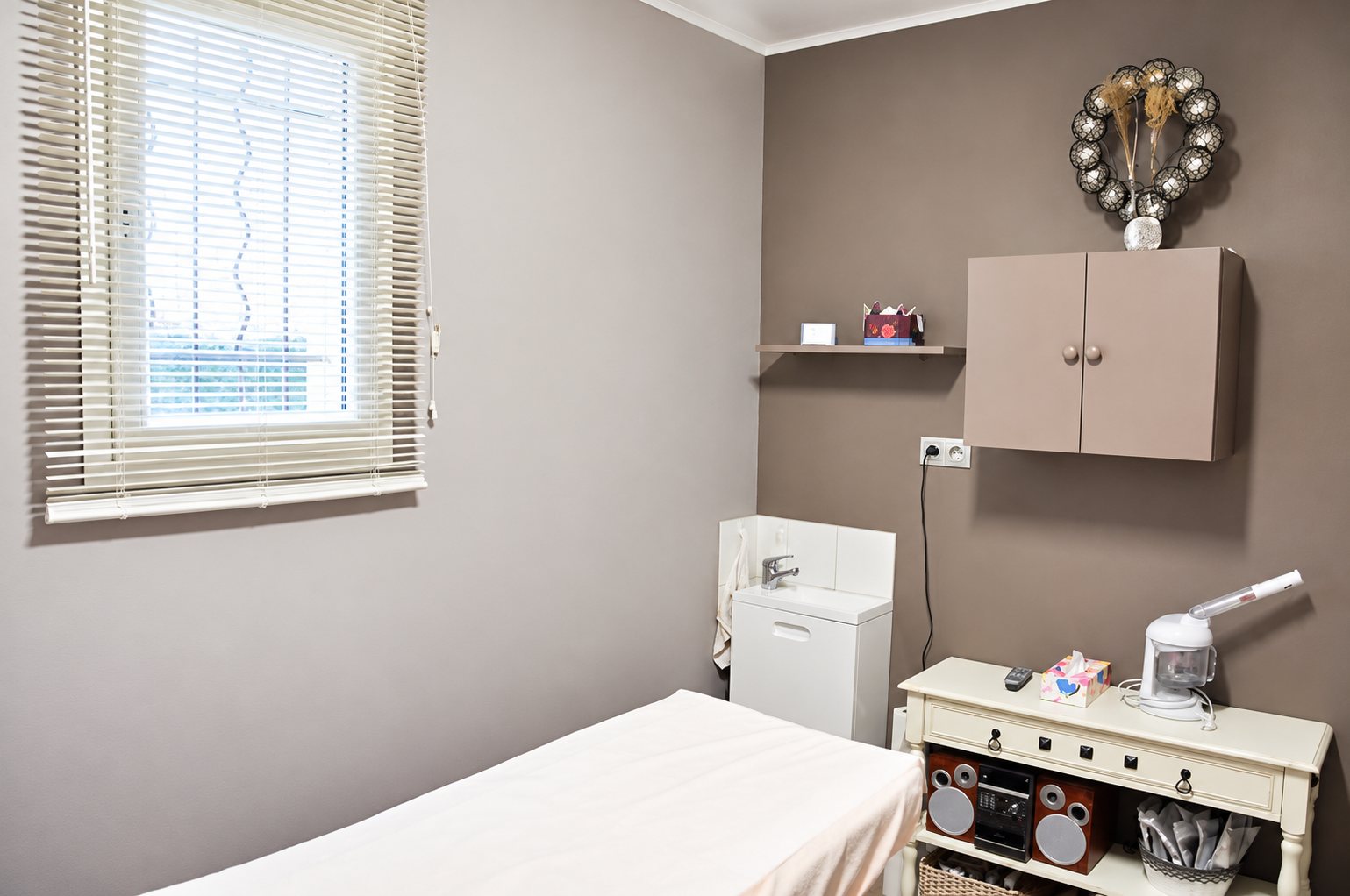 Cabine de soins aux murs taupe avec table de massage, lavabo et appareil à vapeur